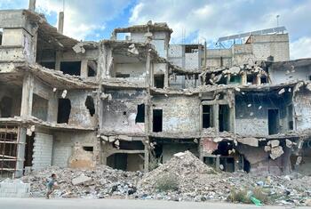 A child runs past piles of rubble in front of heavily damaged buildings in Homs, Syria, during a UNICEF field visit on October 7, 2025.