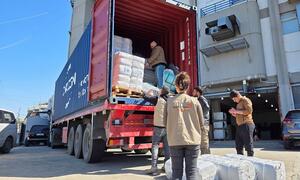 Trabajadores humanitarios descargan suministros humanitarios de un gran contenedor de transporte a un camión rojo en el Líbano, marzo de 2026. Los trabajadores, vestidos con chalecos de World Vision, están distribuyendo ayuda a familias desplazadas por el conflicto.