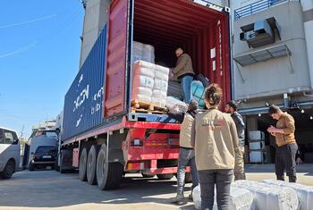 Des travailleurs humanitaires déchargent des fournitures humanitaires d'un gros conteneur d'expédition sur un camion rouge au Liban, en mars 2026. Les travailleurs, vêtus de gilets World Vision, distribuent de l'aide aux familles déplacées par le conflit.