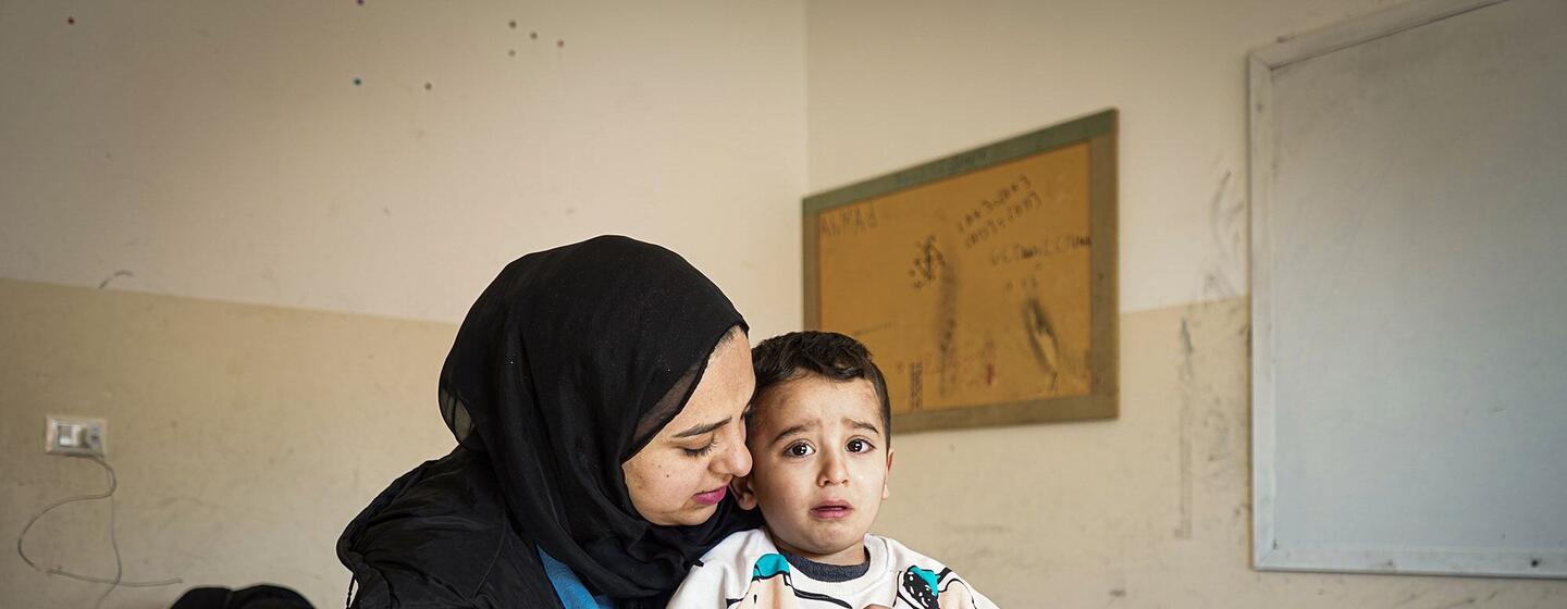 Sahar, une libanaise déplacée à l'intérieur du pays, âgée de 28 ans, tient son fils de 4 ans, Mohammad, dans une salle de classe où leur famille s'abrite dans le district de Chouf, dans le gouvernorat du mont Liban. L'image dépeint le coût émotionnel du déplacement et les conditions de vie difficiles auxquelles sont confrontées les familles dans les refuges collectifs.