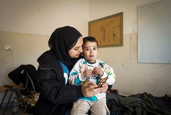 Sahar, a 28-year-old internally displaced Lebanese woman, holds her 4-year-old son Mohammad in a classroom where their family is sheltering in Chouf District, Mount Lebanon Governorate. The image depicts the emotional toll of displacement and the difficult living conditions faced by families in collective shelters.