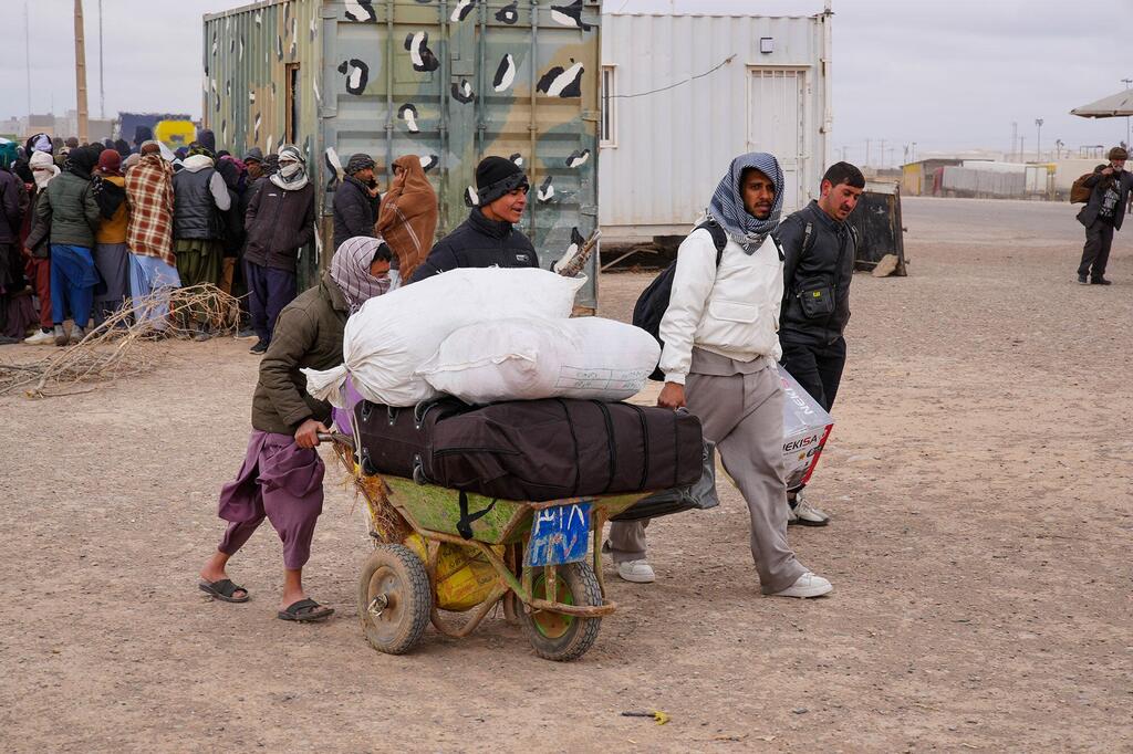 Afganos recién retornados caminando a través del área de registro en el cruce fronterizo de Islam Qala, llevando sus pertenencias en una carretilla.