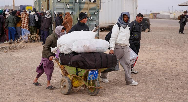 Афганцы, недавно вернувшиеся из Афганистана, проходят через зону регистрации на пограничном переходе Ислам Кала, неся свои вещи на тележке.