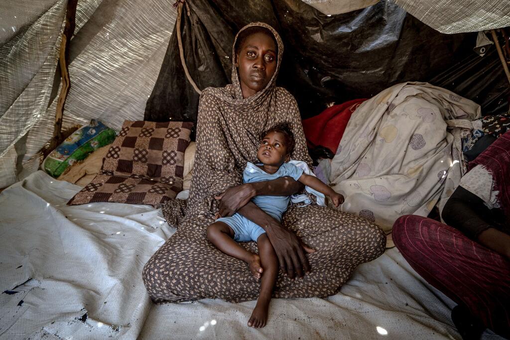 A woman who fled fighting in El Fasher, holds her daughter who was recently treated for malnutrition.