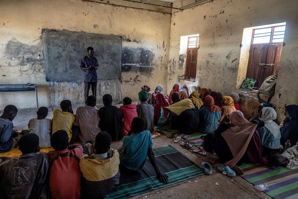 Estudiantes y un maestro se reúnen para una clase matutina en una escuela de Khazan Tunjur, en el norte de Darfur, Sudán. Los niños, muchos de ellos desplazados por el conflicto desde la cercana localidad de El Fasher, se sientan en el suelo sobre las esteras escuchando al maestro frente a la pizarra. (Foto de Giles Clarke/OCHA)