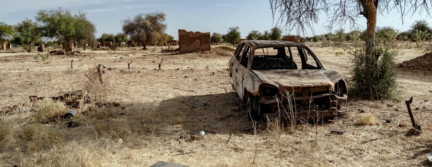 La carcasse calcinée d'une voiture et des maisons en torchis détruites dans le village abandonné d'Al Bakri, dans le Darfour du Nord, au Soudan, illustrant les conséquences du conflit et des déplacements.