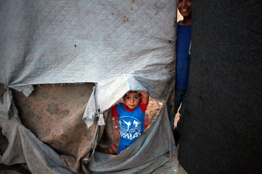 Un niño de corta edad mira a través del lateral rasgado de un refugio en la Franja de Gaza.