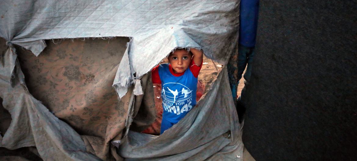 Um menino olha para a lateral de um abrigo desabado na Faixa de Gaza.