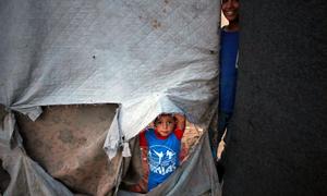 Un petit garçon regarde à travers le côté déchiré d’un abri dans la bande de Gaza.