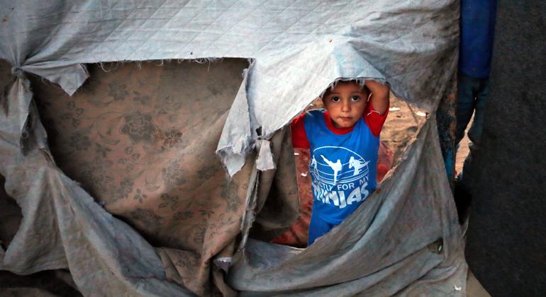 Uma criança espia através da lateral rasgada de um abrigo na Faixa de Gaza