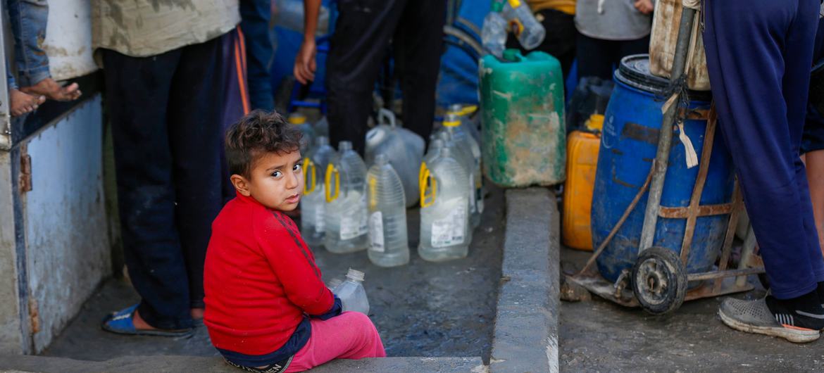 Un niño sentado junto a un punto de agua en Gaza.