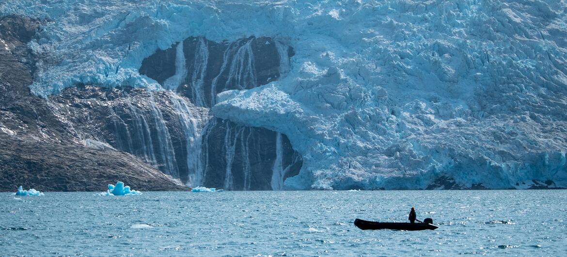 Un kayakista solitario paga cerca de un glaciar masivo en Groenlandia, con agua derretida en cascada por la superficie del hielo.