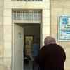 Una mujer en hijab camina hacia la entrada del Centro de Salud de la UNRWA en Jerusalén, que cuenta con una señal que indica su apoyo del Reino de Arabia Saudita y sus diversos departamentos, incluyendo farmacia y laboratorio.