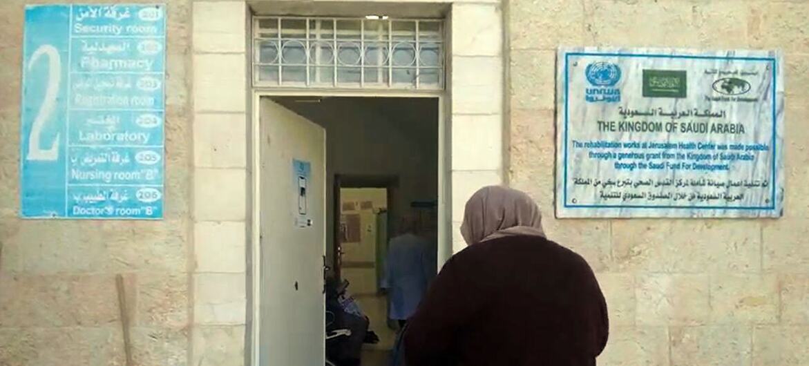 Une femme en hijab se dirige vers l'entrée du centre de santé de l'UNRWA à Jérusalem, qui a une pancarte indiquant son soutien du Royaume d'Arabie saoudite et de ses divers départements, y compris la pharmacie et le laboratoire.