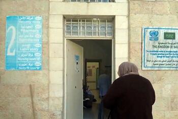 Une femme en hijab se dirige vers l'entrée du centre de santé de l'UNRWA à Jérusalem, qui a une pancarte indiquant son soutien du Royaume d'Arabie saoudite et de ses divers départements, y compris la pharmacie et le laboratoire.