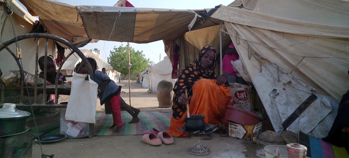 امرأة وطفل يعيشان في خيمة مؤقتة في مخيم للاجئين في السودان. المرأة تطبخ على نار صغيرة على الأرض.