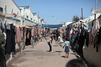 Palestinian children play in a makeshift shelter in Gaza, with clothes hanging to dry on lines between tents.