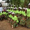 Kundi la wanawake waliovaa mashati ya kijani na sketi zenye muundo wakipiga picha nje nchini Liberia. Mwanamke aliyevaa top nyeupe na kifuniko cha kichwa amesimama nyuma.