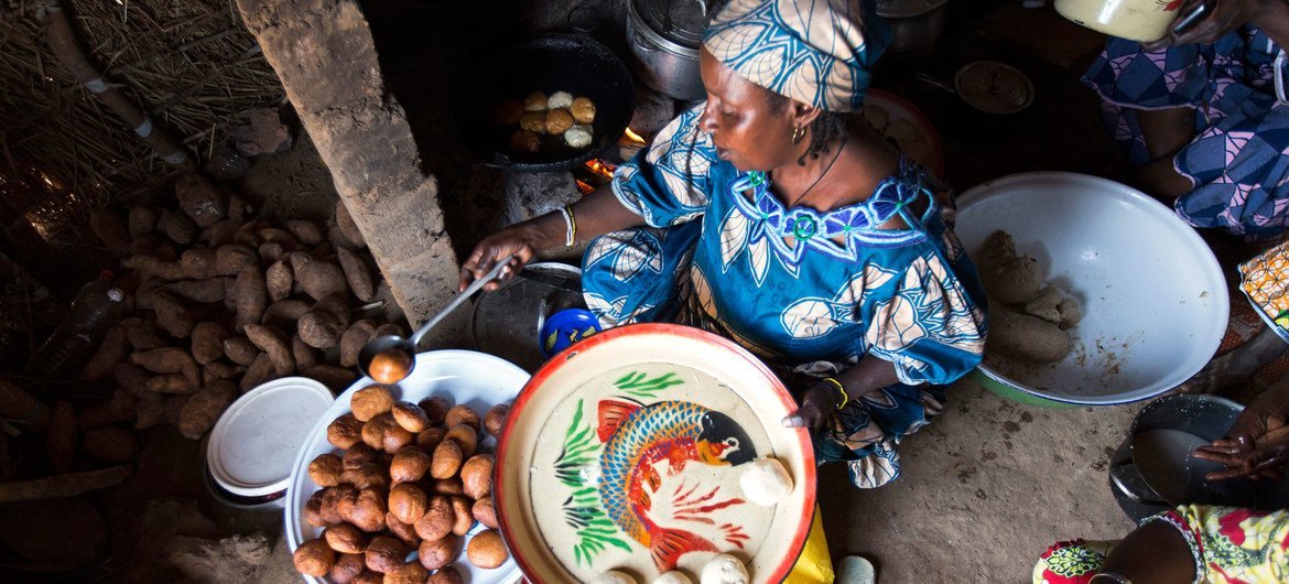 मध्य अफ़्रीकी गणराज्य की एक शरणार्थी महिला, जो कैमेरून में रह रही है, अपने सामान के ग्राहकों के लिये खाद्य पदार्थ तैयार करते हुए.