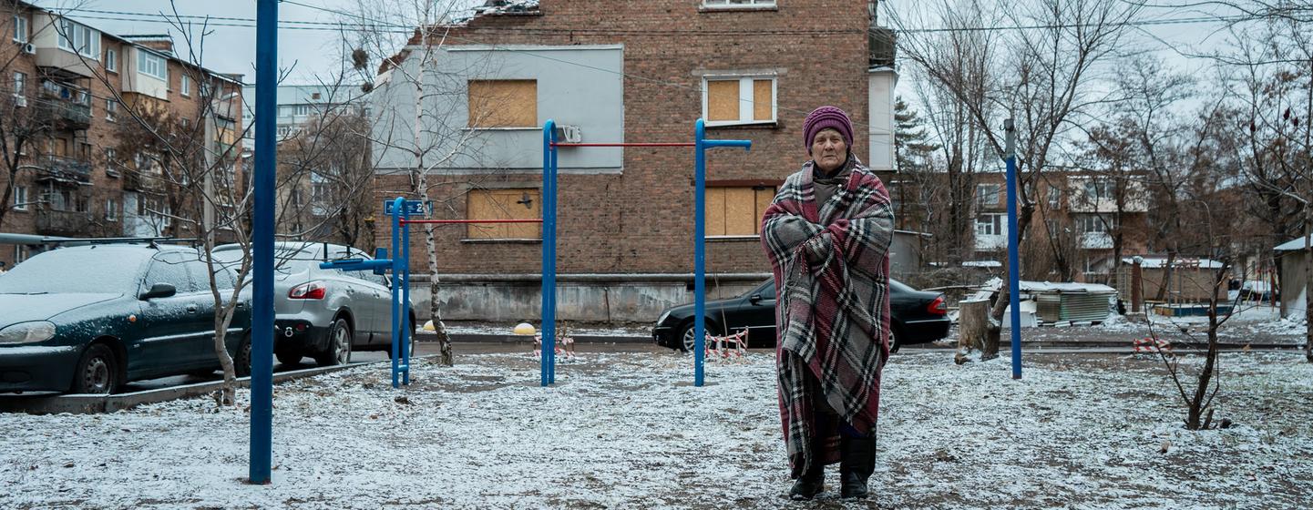 Une femme âgée se tient dans une cour enneigée devant un bâtiment en briques partiellement détruit à Kharkiv, en Ukraine.