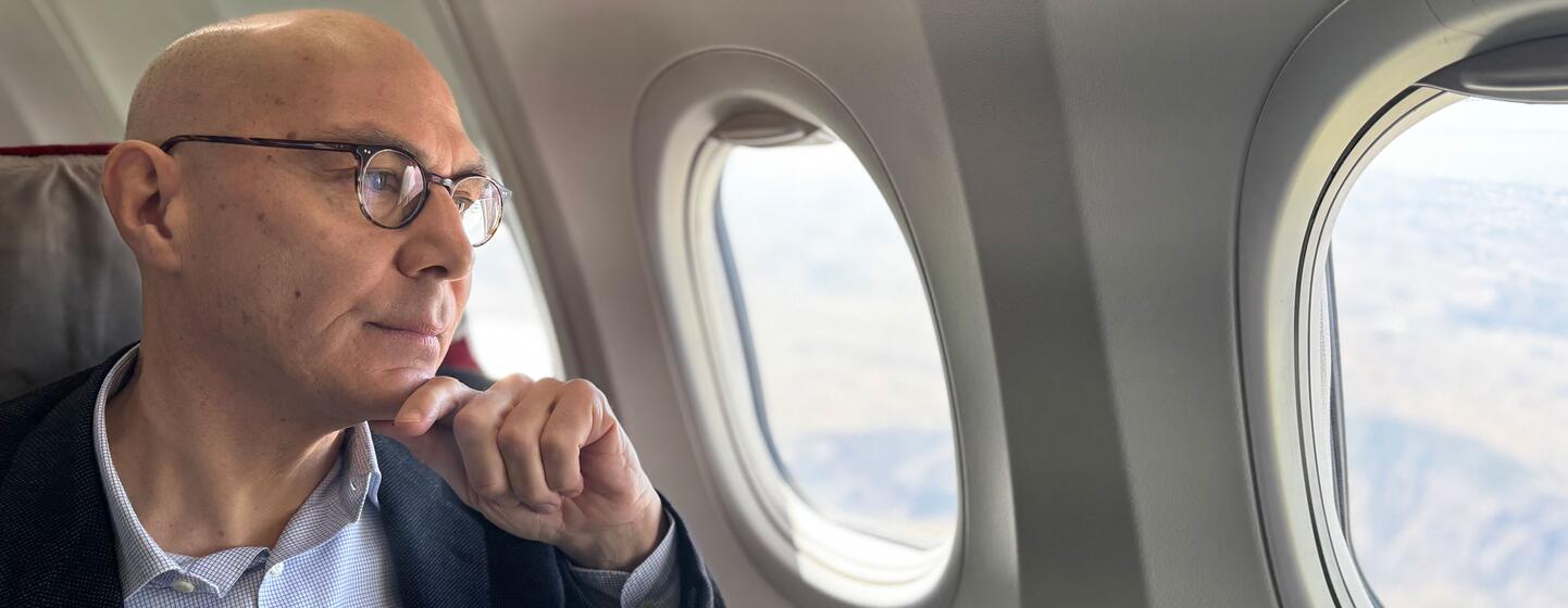 Volker Türk, sentado por uma janela de avião, olhando cuidadosamente para a paisagem abaixo enquanto o avião voa sobre o Chifre da África em direção ao Sudão.