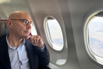Volker Türk, sentado por uma janela de avião, olhando cuidadosamente para a paisagem abaixo enquanto o avião voa sobre o Chifre da África em direção ao Sudão.