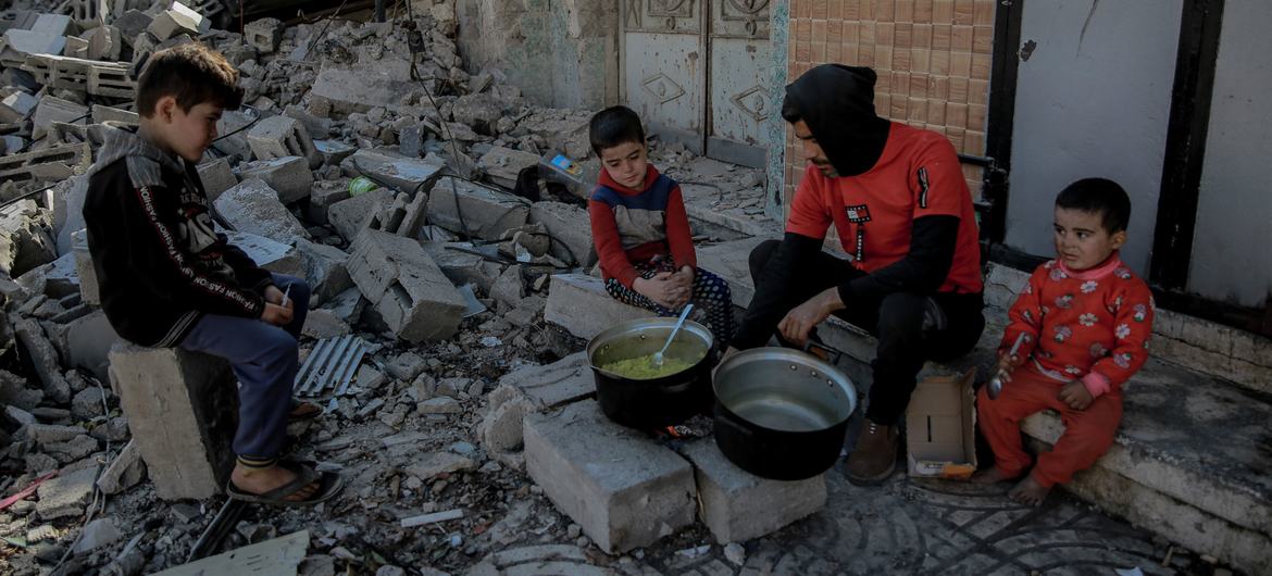A man cooks food for his children over a wood fire in front of his destroyed home in an area west of Gaza City.