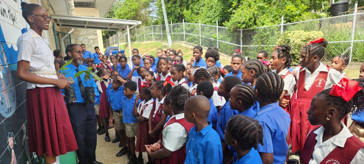 Anthurium Lewis, an archer from Tobago, speaks to a group of school children in uniform about the Sustainable Development Goals (SDGs), holding a small potted plant.