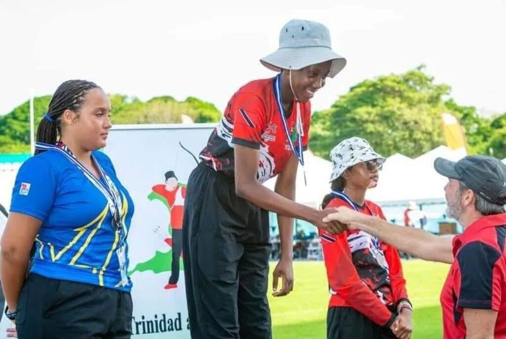 Female archer Anthurium Lewis from Tobago, Trinidad and Tobago, receiving a medal on a podium at an archery event.