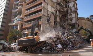 Heavy machinery clears rubble from a building destroyed by airstrikes in Beirut, Lebanon. Workers in safety gear are present at the site of the recent destruction.