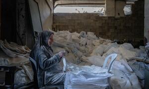 Malye, a Palestinian woman, sits in a workshop in Gaza City surrounded by white flour bags, smiling as she embroiders them into new bags and shade structures through a WFP cash-for-work program.
