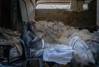Malye, a Palestinian woman, sits in a workshop in Gaza City surrounded by white flour bags, smiling as she embroiders them into new bags and shade structures through a WFP cash-for-work program.