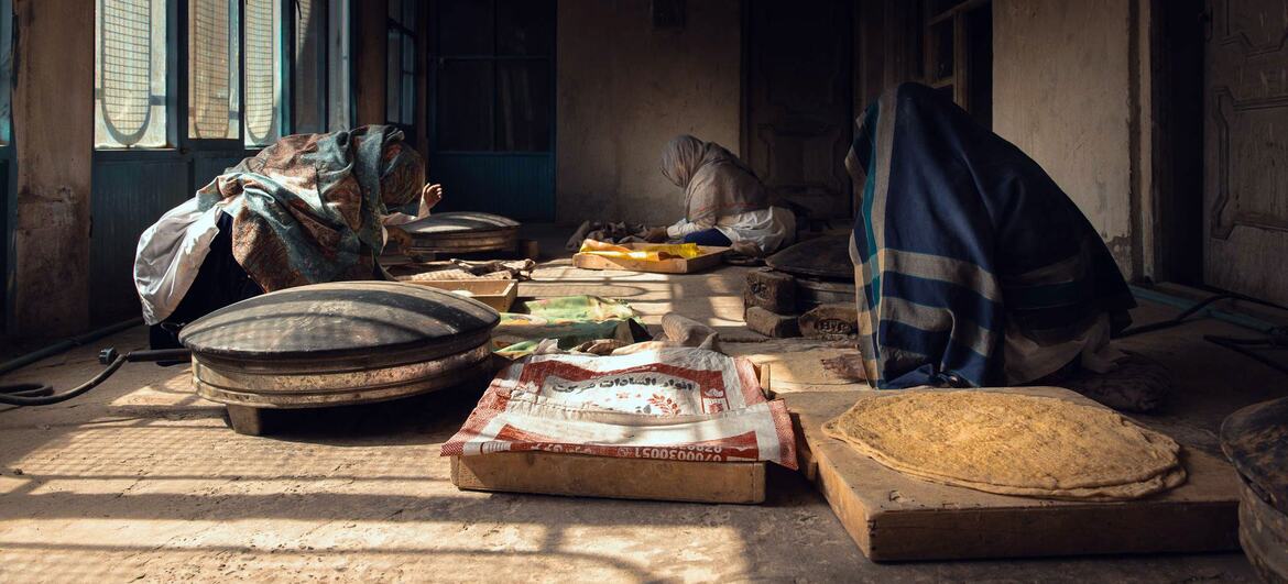 Mujeres amasan masa y hornean pan en una panadería con poca luz en Kandahar, Afganistán.