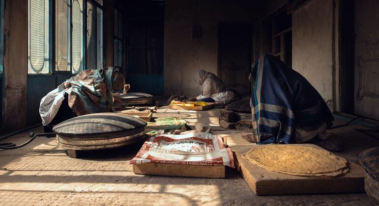 Mulheres amassam massa e assam pão em uma padaria pouco iluminada em Kandahar, no Afeganistão.
