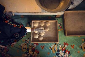 Una mujer con un vestido tradicional oscuro y guantes amasa la masa formando bolas sobre una bandeja en una panadería de Kandahar, Afganistán.