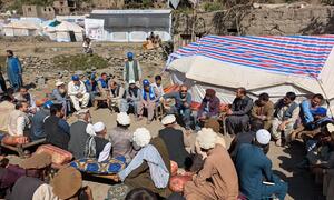 संयुक्त राष्ट्र-हैबिटेट और यूनिसेफ के प्रतिनिधियों का अफगान पुरुषों के साथ शरणार्थी शिविर में मिलन हुआ है, जिसकी पृष्ठभूमि में संयुक्त राष्ट्र के तंबू दिखाई दे रहे हैं।