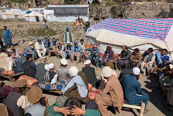 संयुक्त राष्ट्र-हैबिटेट और यूनिसेफ के प्रतिनिधियों का अफगान पुरुषों के साथ शरणार्थी शिविर में मिलन हुआ है, जिसकी पृष्ठभूमि में संयुक्त राष्ट्र के तंबू दिखाई दे रहे हैं।