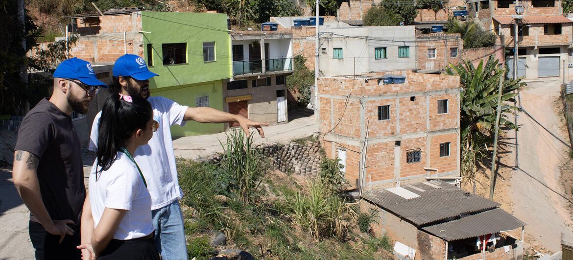 Trois personnes portant des casquettes bleues d'ONU-Habitat se tiennent sur une colline surplombant un habitat informel à Izidora, à Belo Horizonte, au Brésil, lors d'une visite sur le terrain.