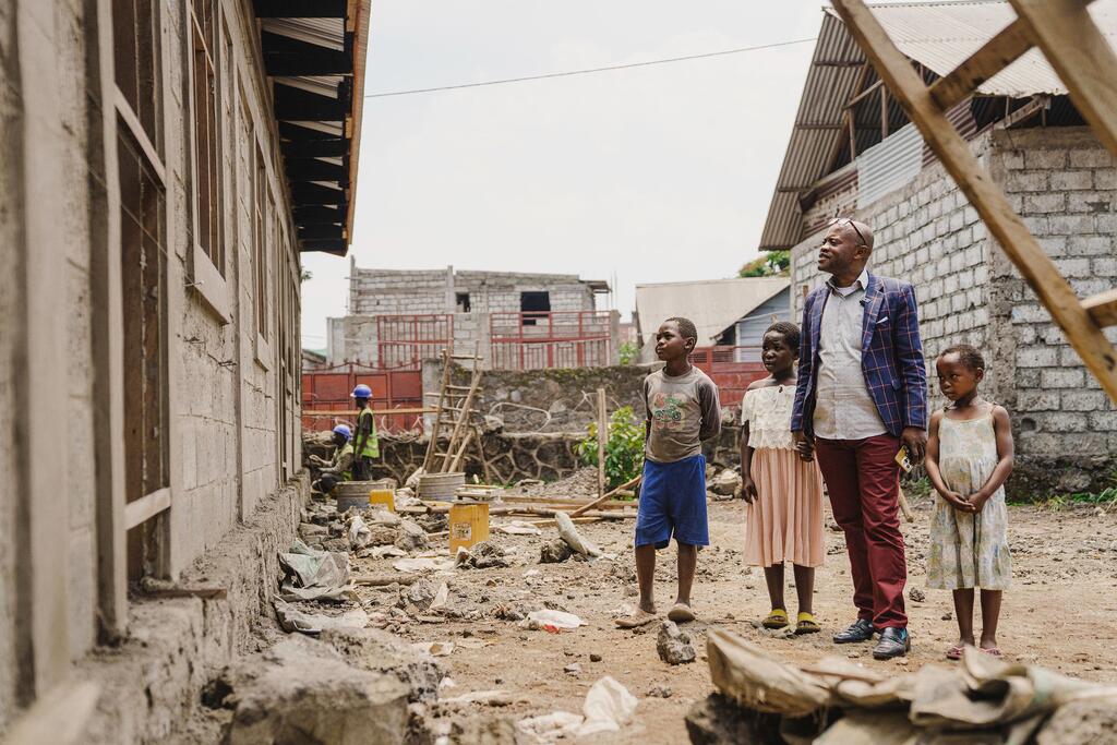 Samson Malira, headteacher, stands with students Kennedy, Asifiwe, and Josiane at the construction site of new classrooms and latrines at Mabanga Primary School in Goma, DR Congo.