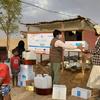 A UNFPA and UNICEF aid worker hands a box of supplies to a man at a distribution point in Al Jawf Governorate, Yemen. Children and women observe the distribution of relief items.