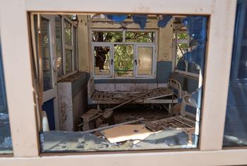 A view through a broken window into a destroyed ward at Al Shaab Hospital in Khartoum, showing debris and damaged beds.