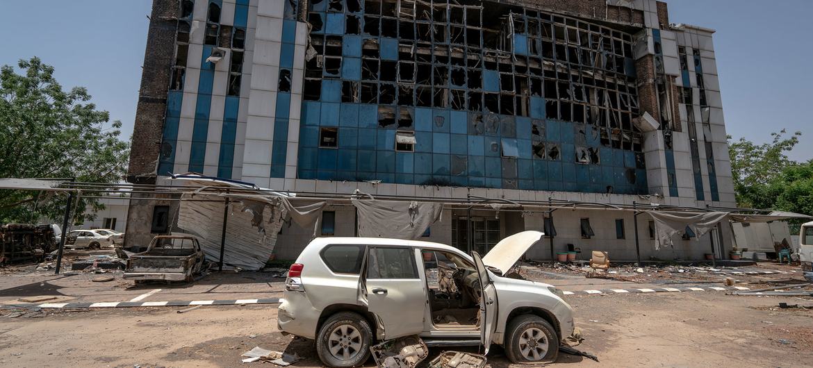 مبنى مفوضية المساعدات الإنسانية السابق المتضرر في الخرطوم، السودان، مع سيارة محترقة في المقدمة.