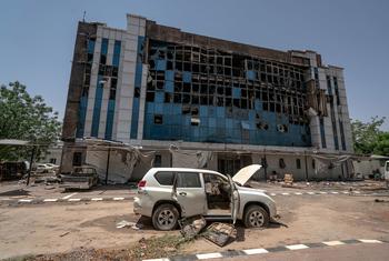 مبنى مفوضية المساعدات الإنسانية السابق المتضرر في الخرطوم، السودان، مع سيارة محترقة في المقدمة.