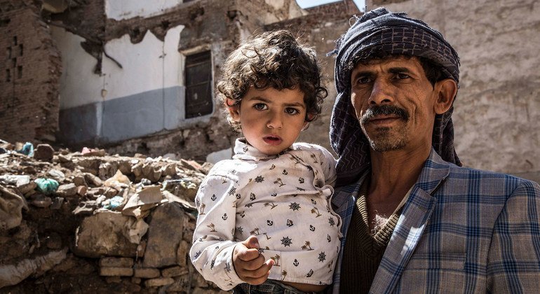 A father holds his daughter while standing in front of a destroyed building in Sana’a, Yemen.