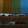 Fotógrafos y personal de los medios de comunicación en la tribuna de prensa del edificio de la ONU , con una colorida fachada a rayas visible al fondo.