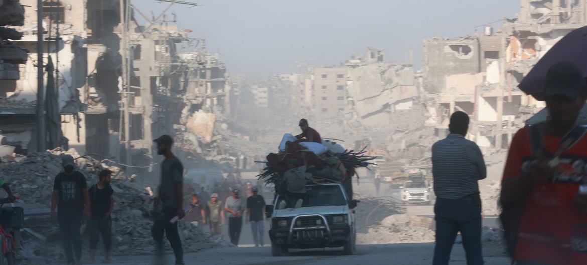 People stand in the shadows of destroyed buildings in the Gaza Strip.
