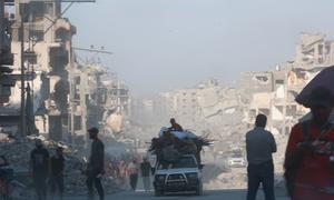 La gente se encuentra a la sombra de edificios destruidos en la Franja de Gaza.