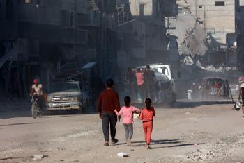 一名男人带着两名儿童行走在加沙城残破的街道上。