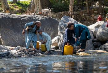 Afghan man and boys in traditional clothing collect water from a rocky mountain stream using yellow jerrycans after the earthquake displaced their family to temporary shelters in Kunar province.