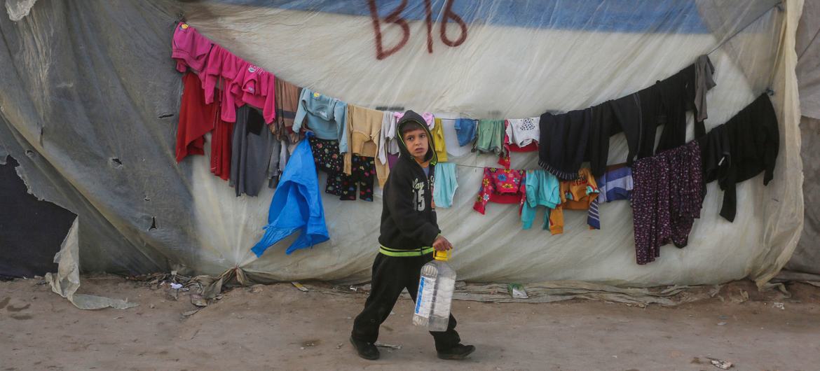 A young boy passes by a shelter on the way to collect water.